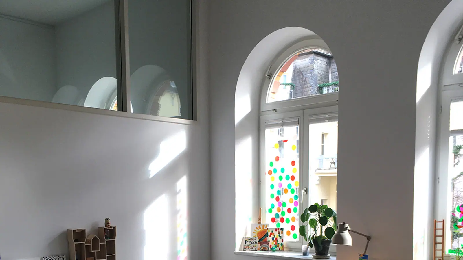 Heller Praxisraum mit hohen Altbau-Rundbogenfenstern und bunter Kinder-Fensterdeko.