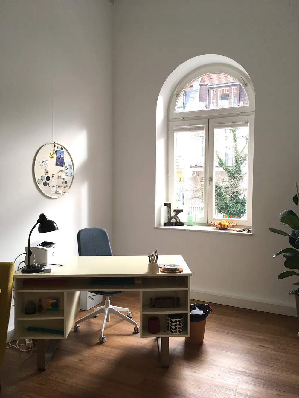Ruhiger Gesprächsraum mit Schreibtisch, blauem Stuhl und rundem Fenster im Bogen.