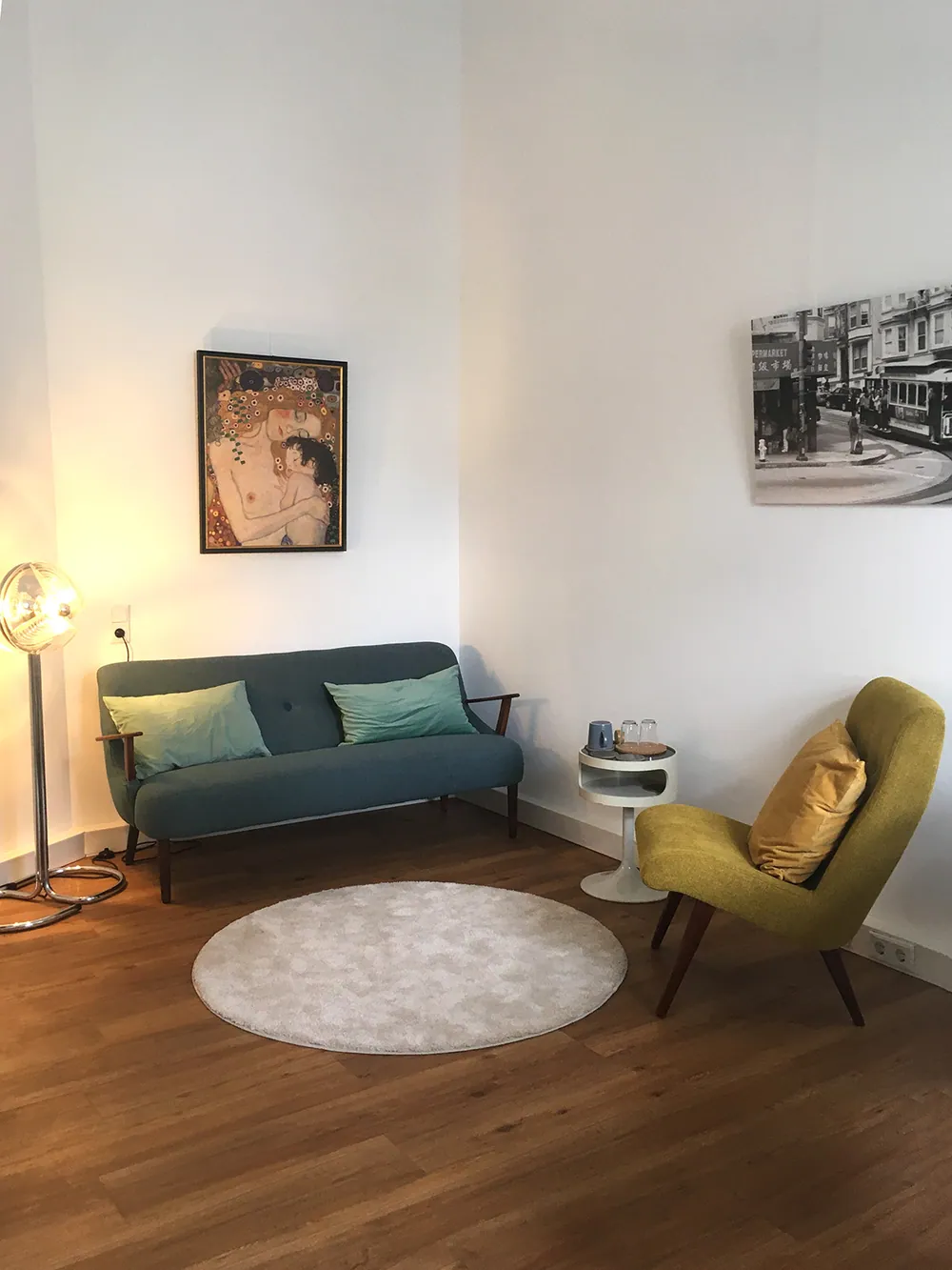 Ruhige Sitzecke mit petrolfarbenem Sofa, mintgrünen Kissen und warmem Holzboden.